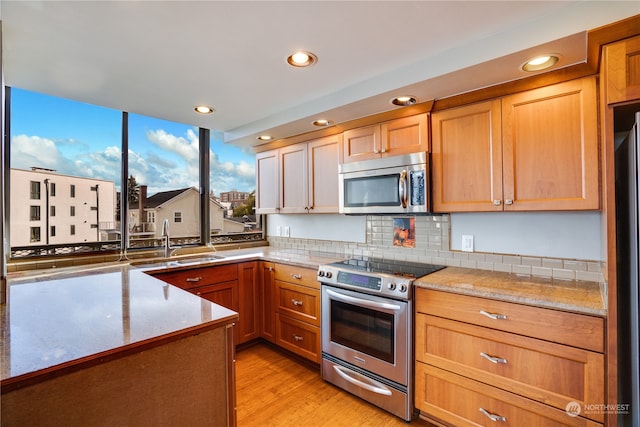 kitchen featuring appliances with stainless steel finishes, light wood-type flooring, tasteful backsplash, light stone counters, and sink