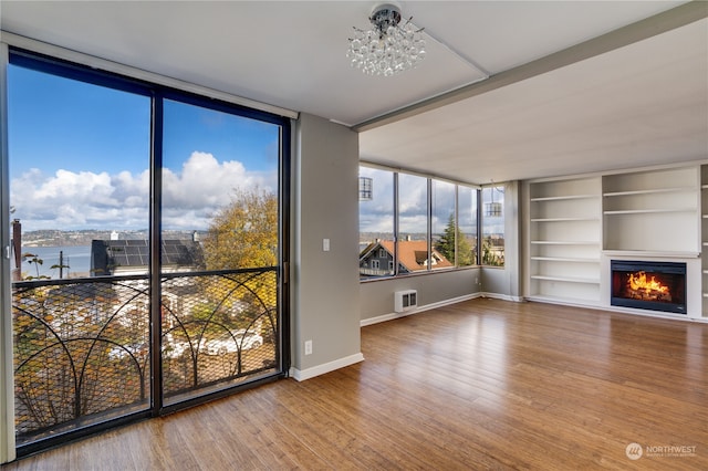 unfurnished living room featuring a chandelier, wood-type flooring, a water view, and floor to ceiling windows