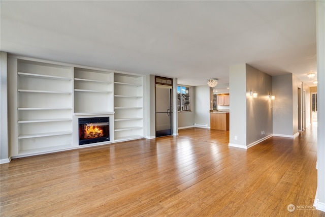 unfurnished living room featuring built in shelves and light wood-type flooring