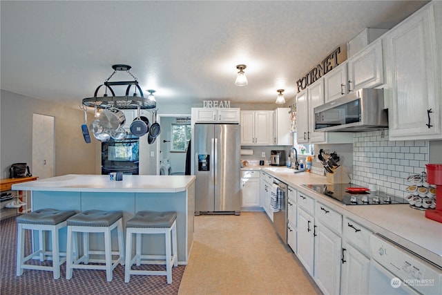 kitchen featuring appliances with stainless steel finishes, white cabinetry, sink, a kitchen bar, and decorative backsplash