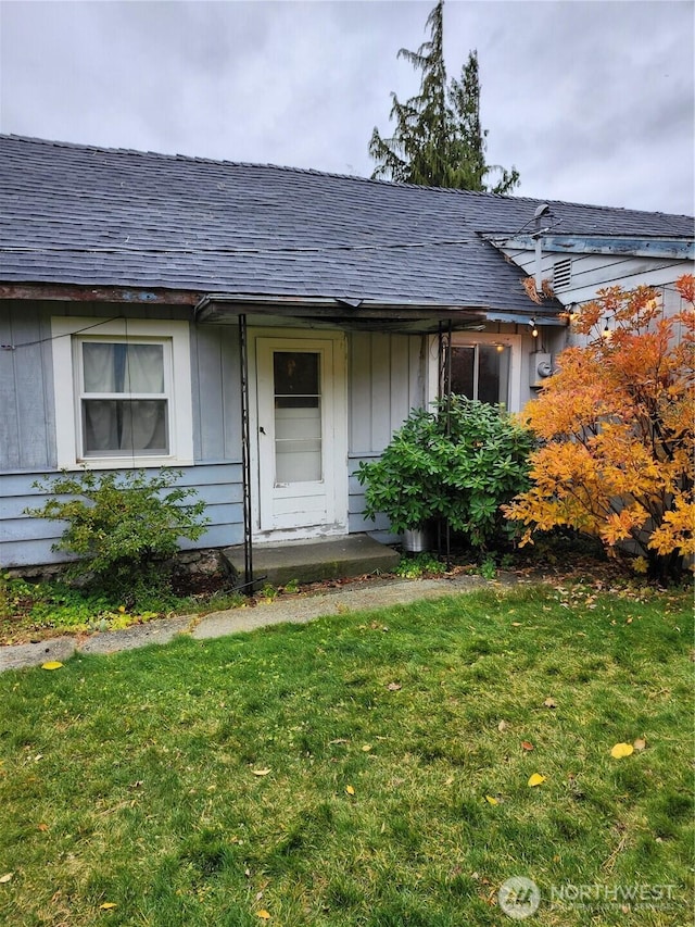 property entrance with a lawn, board and batten siding, and a shingled roof