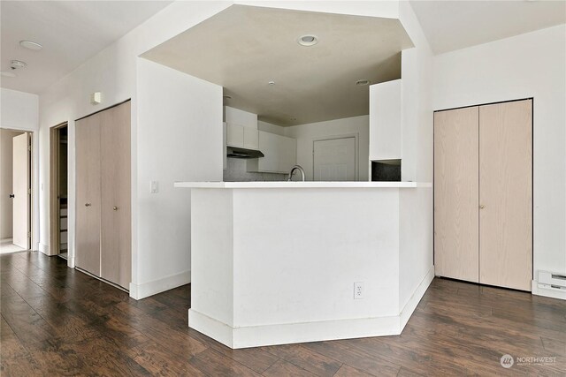 kitchen with sink, dark hardwood / wood-style flooring, a baseboard heating unit, kitchen peninsula, and white cabinets