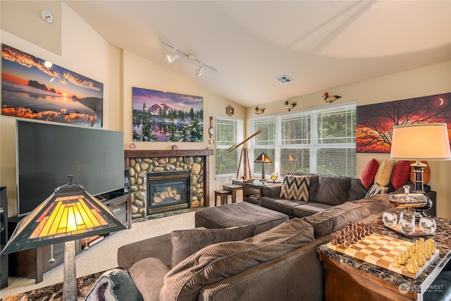 living room with carpet flooring, track lighting, a stone fireplace, and lofted ceiling