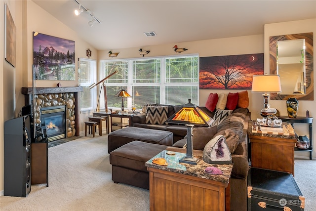 living room featuring rail lighting, a fireplace, lofted ceiling, and light carpet