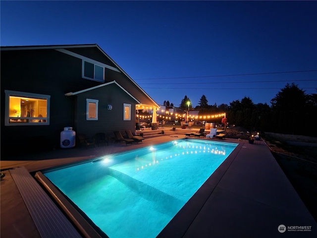 pool at night featuring a patio area