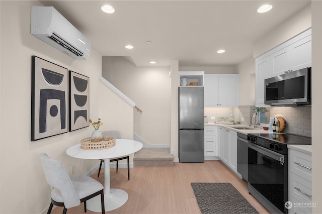 kitchen with a wall mounted AC, white cabinets, light wood-type flooring, and appliances with stainless steel finishes