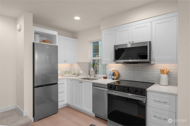 kitchen featuring appliances with stainless steel finishes, backsplash, sink, light hardwood / wood-style flooring, and white cabinets