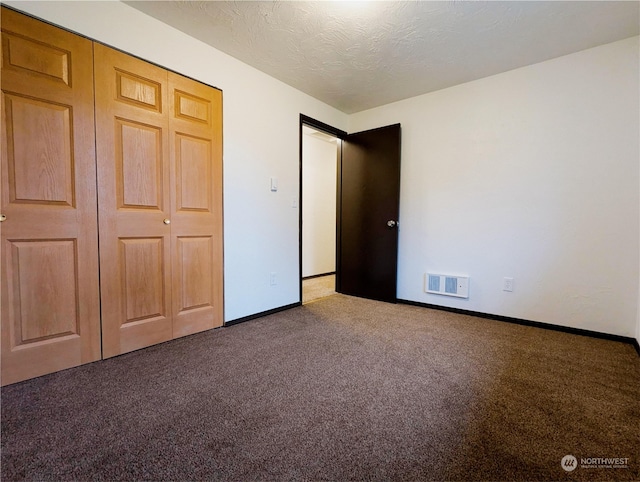 unfurnished bedroom featuring dark colored carpet, a textured ceiling, and a closet