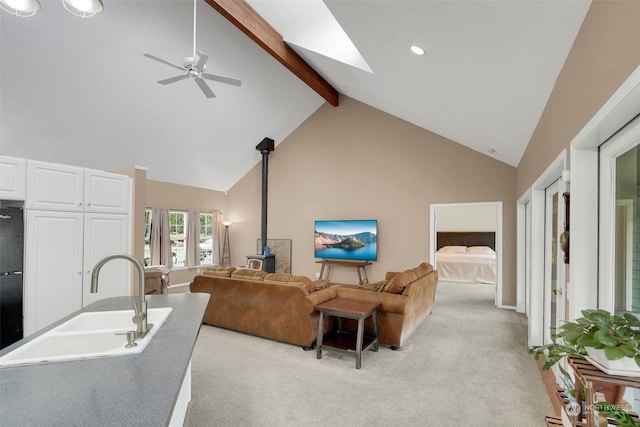 living room featuring light carpet, sink, beam ceiling, high vaulted ceiling, and a wood stove