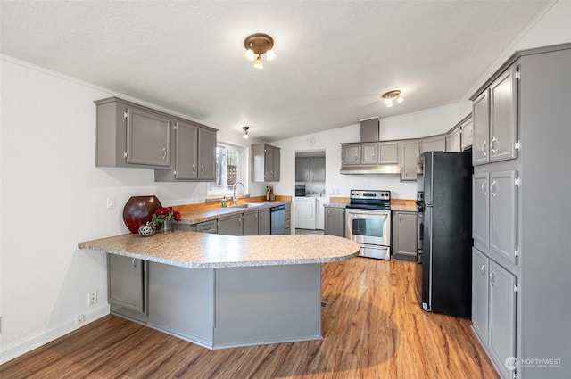 kitchen featuring washing machine and clothes dryer, kitchen peninsula, hardwood / wood-style floors, and appliances with stainless steel finishes