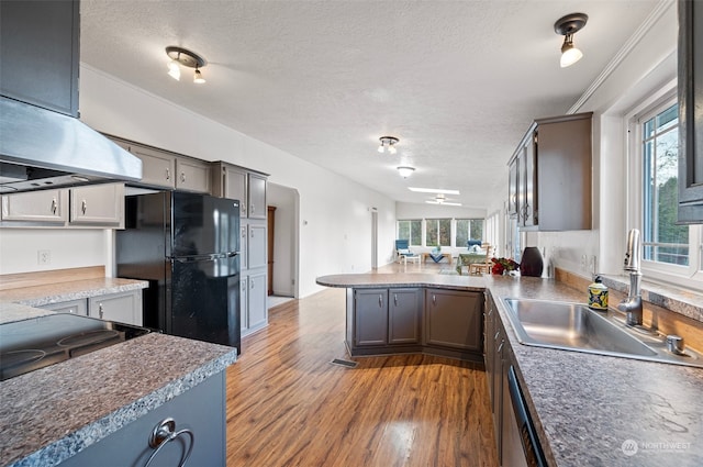 kitchen featuring black refrigerator, kitchen peninsula, a textured ceiling, sink, and wood-type flooring