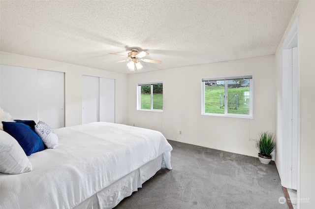 carpeted bedroom featuring ceiling fan, a textured ceiling, and multiple closets