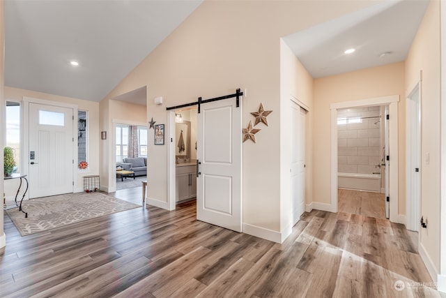 entrance foyer featuring light wood-type flooring, a barn door, and high vaulted ceiling