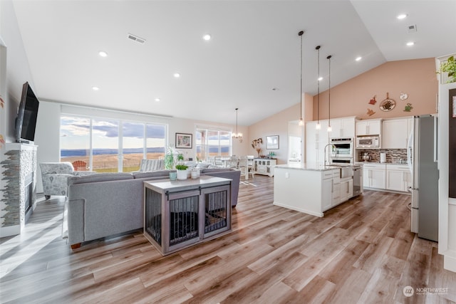 kitchen with appliances with stainless steel finishes, pendant lighting, light hardwood / wood-style flooring, white cabinets, and an island with sink