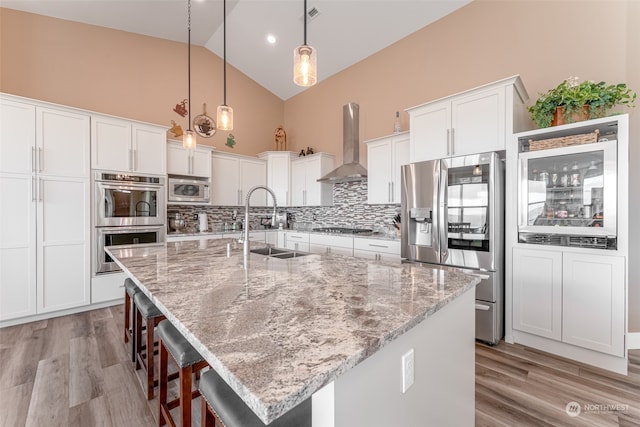 kitchen featuring a spacious island, wall chimney range hood, light stone counters, and appliances with stainless steel finishes