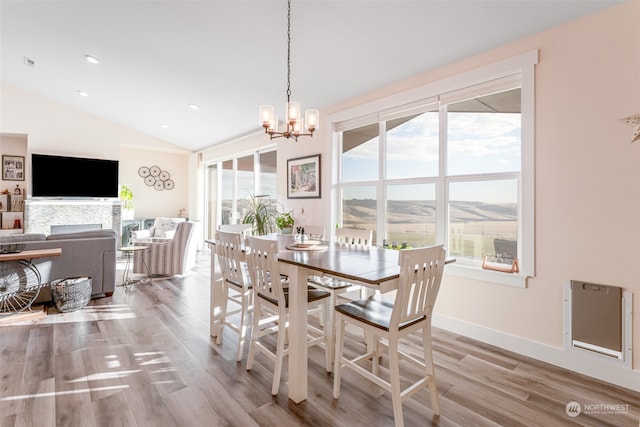 dining space featuring a chandelier, light hardwood / wood-style floors, a fireplace, and vaulted ceiling