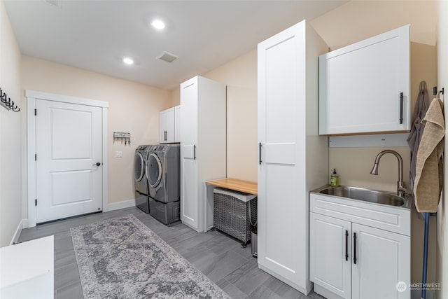 washroom featuring washing machine and clothes dryer, sink, cabinets, and light hardwood / wood-style flooring