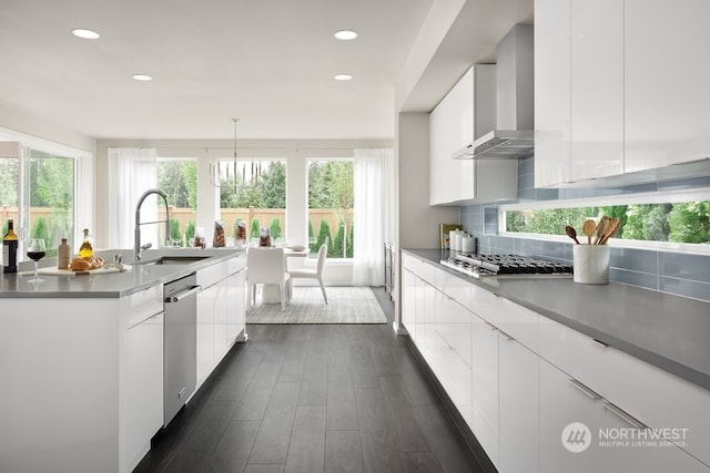 kitchen with wall chimney exhaust hood, stainless steel appliances, sink, pendant lighting, and white cabinets