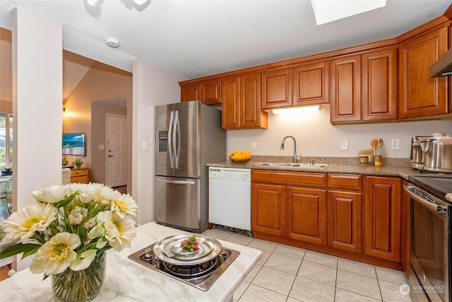 kitchen with lofted ceiling, sink, light stone countertops, light tile patterned floors, and stainless steel appliances