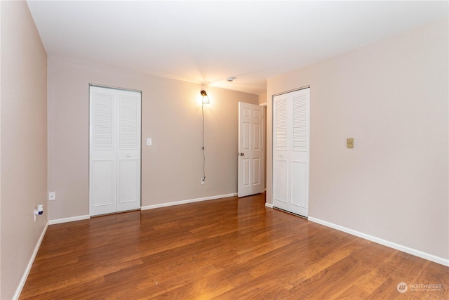 unfurnished bedroom featuring wood-type flooring and two closets