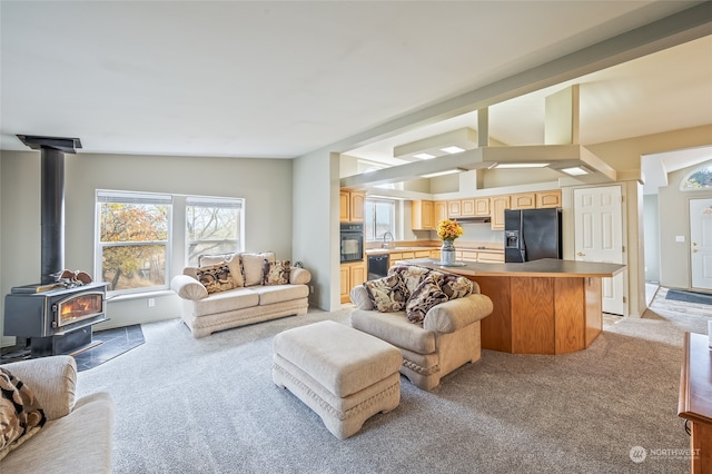 living room featuring light carpet, vaulted ceiling, a wood stove, and sink