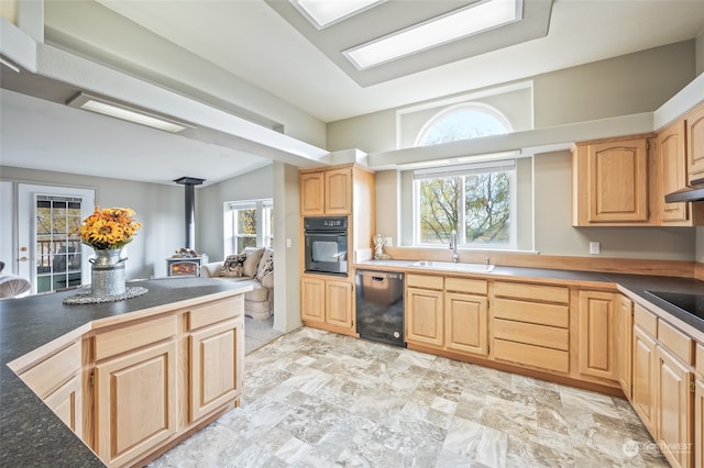 kitchen featuring a wood stove, black appliances, sink, vaulted ceiling, and light brown cabinetry