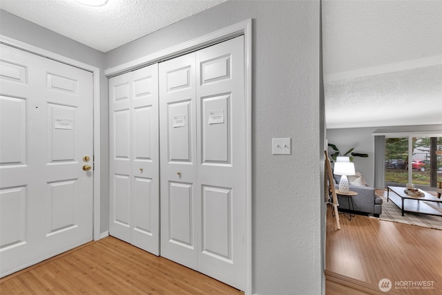 foyer featuring a textured ceiling, a textured wall, and light wood-style flooring