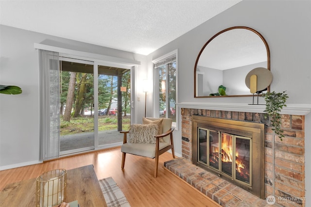 living area featuring a textured ceiling, a fireplace, baseboards, and wood finished floors