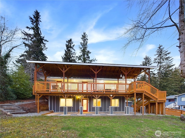 rear view of property with board and batten siding, a yard, stairway, and a wooden deck