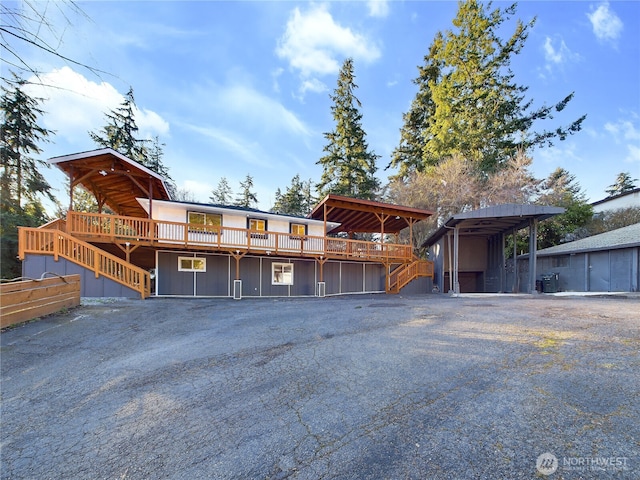 view of front of house with driveway, a wooden deck, and a detached carport