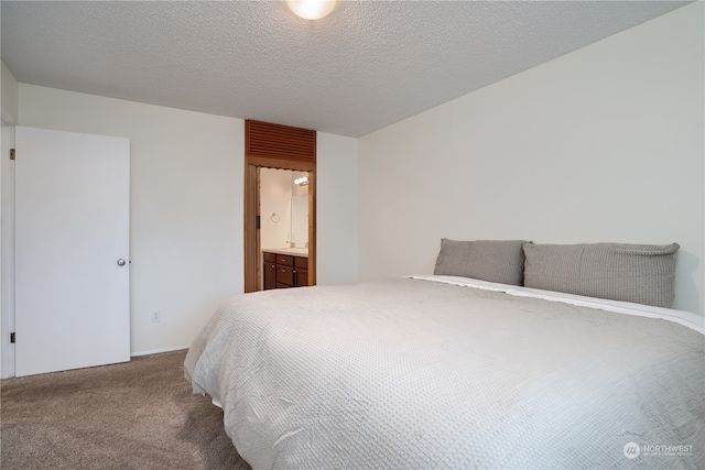 carpeted bedroom with ensuite bathroom and a textured ceiling