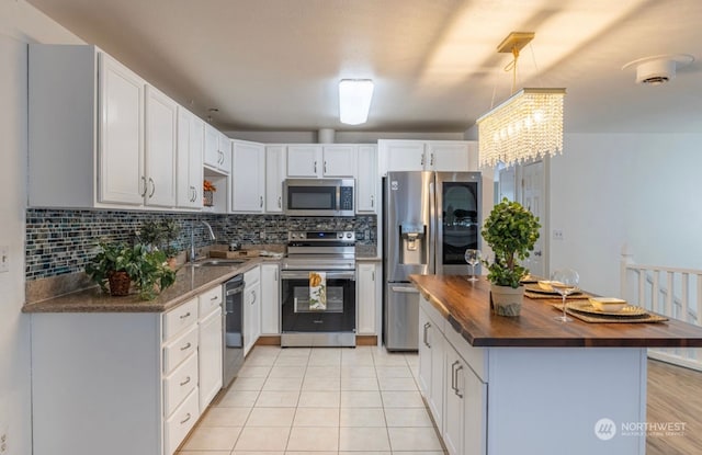 kitchen with butcher block counters, backsplash, sink, white cabinetry, and stainless steel appliances