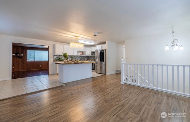 kitchen with white cabinets, light wood-type flooring, hanging light fixtures, and appliances with stainless steel finishes