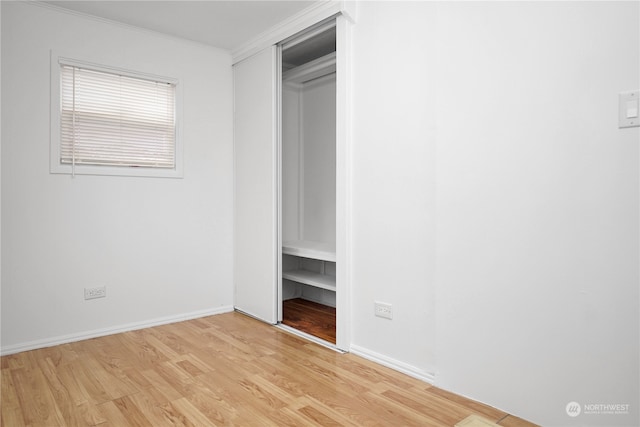 unfurnished bedroom with light hardwood / wood-style floors, crown molding, and a closet