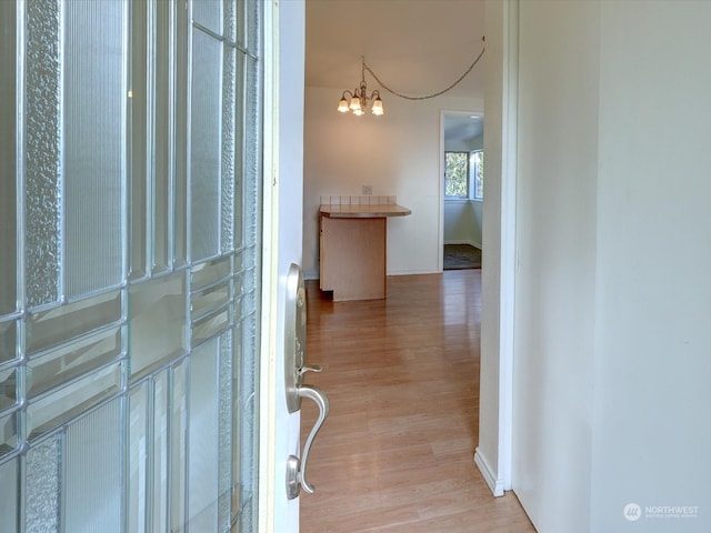 corridor with light hardwood / wood-style flooring and a notable chandelier