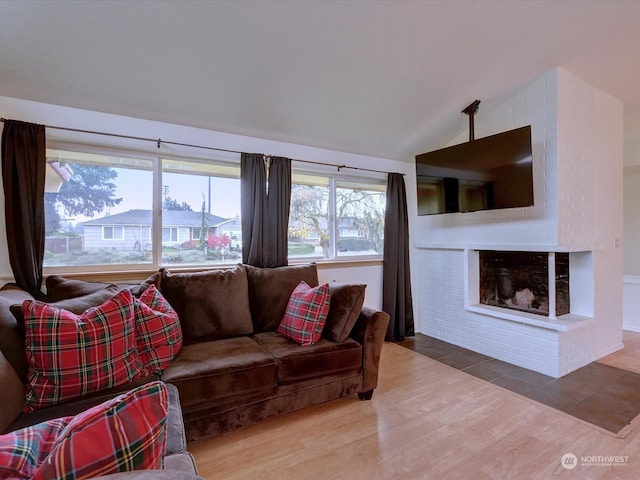 living room featuring vaulted ceiling, wood-type flooring, and a brick fireplace