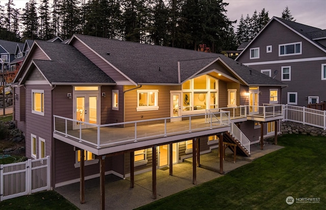 back house at dusk featuring a lawn, a patio, a wooden deck, and french doors