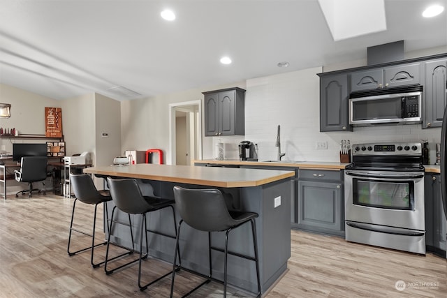 kitchen with gray cabinets, a kitchen island, light wood-type flooring, and stainless steel appliances