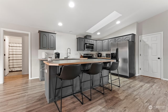 kitchen featuring appliances with stainless steel finishes, gray cabinetry, lofted ceiling with skylight, light hardwood / wood-style flooring, and a kitchen island