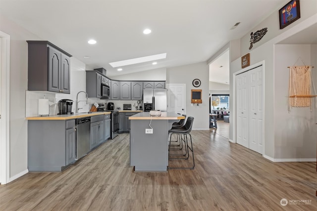 kitchen featuring gray cabinetry, stainless steel appliances, lofted ceiling with skylight, a kitchen island, and butcher block counters