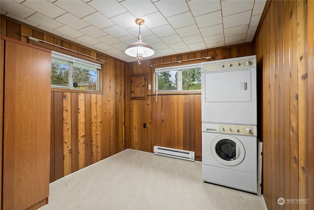 laundry room featuring wood walls, a healthy amount of sunlight, stacked washer / dryer, and a baseboard radiator