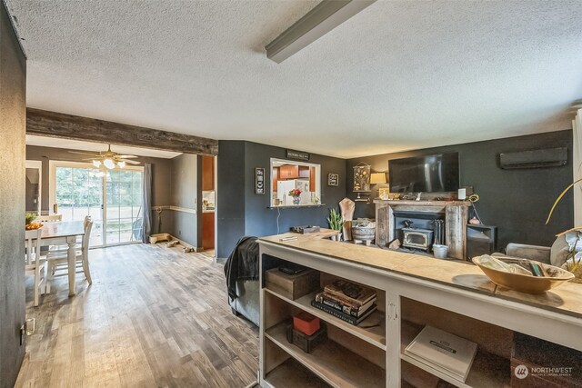 living room with a textured ceiling, a wall mounted AC, ceiling fan, hardwood / wood-style floors, and a wood stove