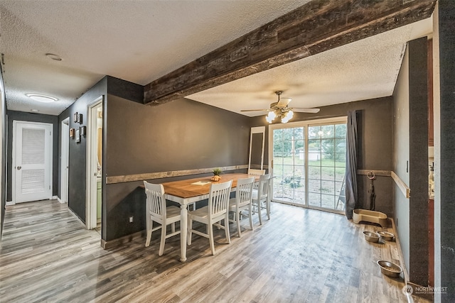 dining area featuring beamed ceiling, ceiling fan, wood-type flooring, and a textured ceiling