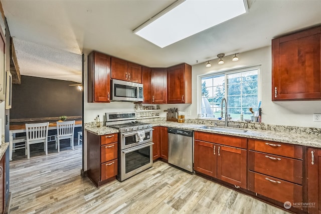 kitchen featuring light stone countertops, a textured ceiling, stainless steel appliances, sink, and light hardwood / wood-style floors