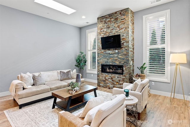 living room with a stone fireplace, a wealth of natural light, light hardwood / wood-style floors, and a skylight