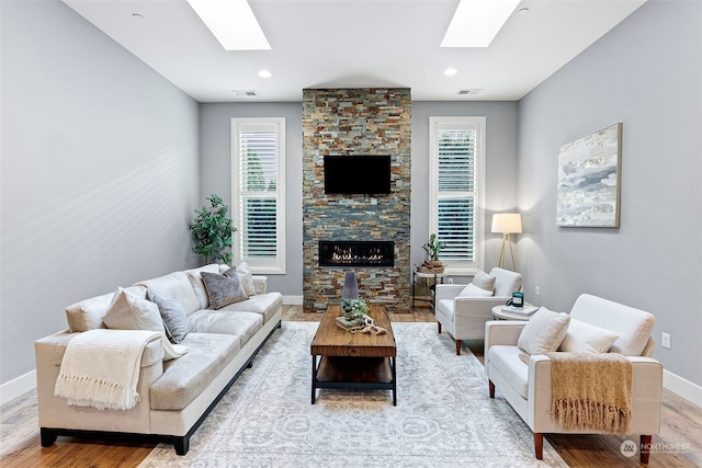 living room with a stone fireplace, light wood-type flooring, and a skylight