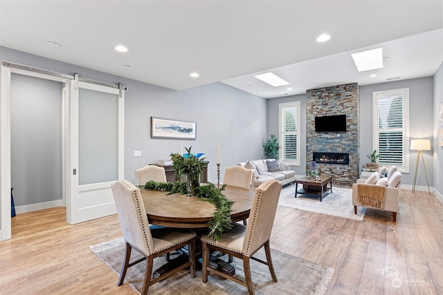 dining area with a fireplace, light hardwood / wood-style flooring, and a skylight