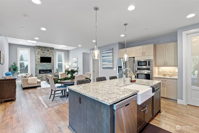 kitchen featuring a kitchen island with sink, hanging light fixtures, a fireplace, appliances with stainless steel finishes, and light hardwood / wood-style floors