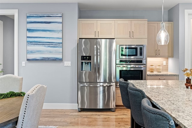 kitchen featuring pendant lighting, light brown cabinets, light hardwood / wood-style floors, light stone counters, and stainless steel appliances