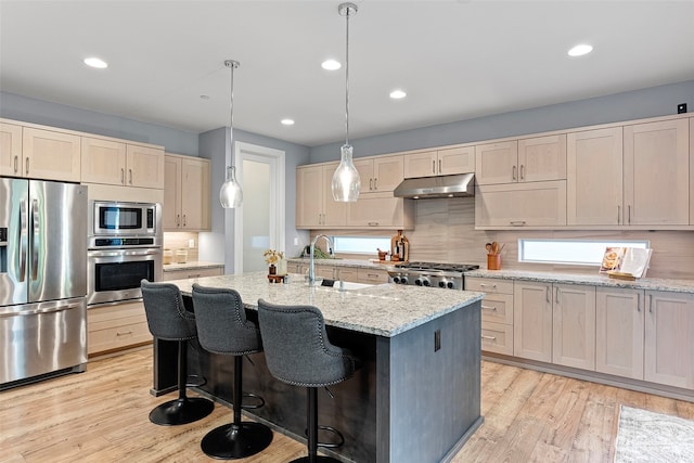 kitchen featuring light stone countertops, a center island with sink, decorative light fixtures, and appliances with stainless steel finishes